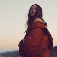 a woman in an orange coat standing on top of a mountain